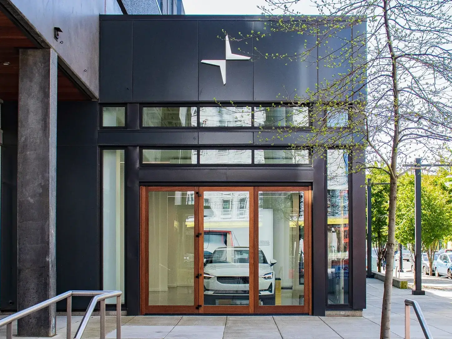 The dark-clad frontage of a car showroom at street level, lit interior and timber-framed entry doors behind full-height glazing