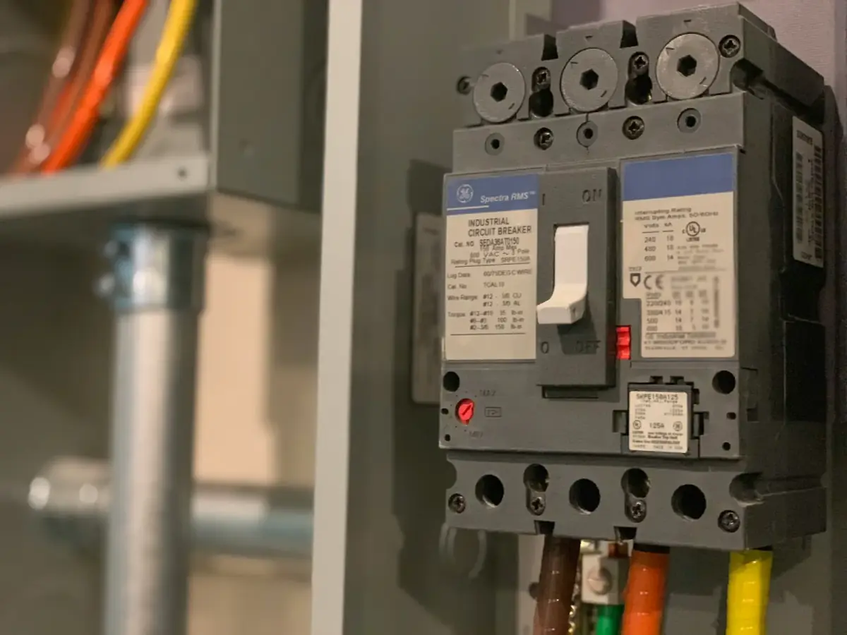 A three-pole molded-case main breaker switched on inside an open switchboard, its rating plug and lug torque data printed on the label