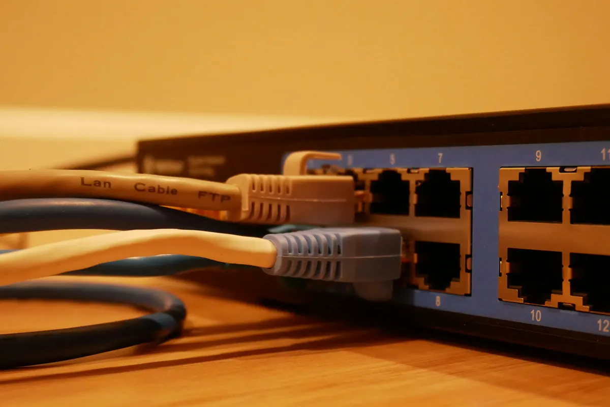 Ethernet patch cables plugged into the numbered ports of a network switch on a timber desk