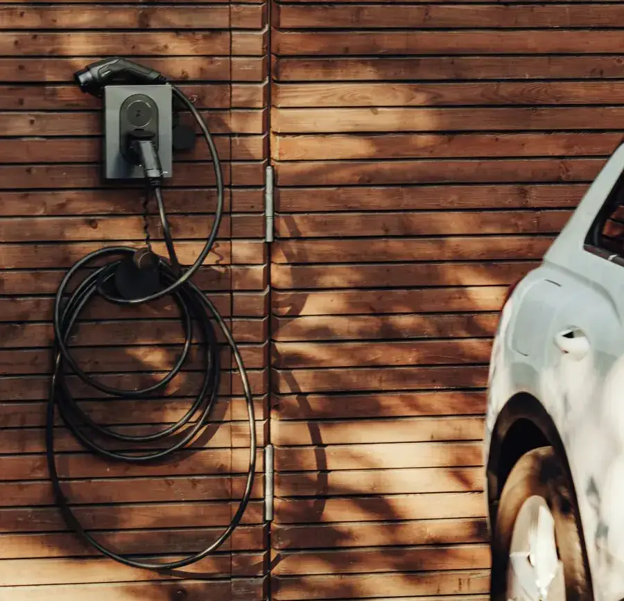 Wall-mounted EV charger with its cable coiled on a timber-clad garage wall, a white electric car parked alongside