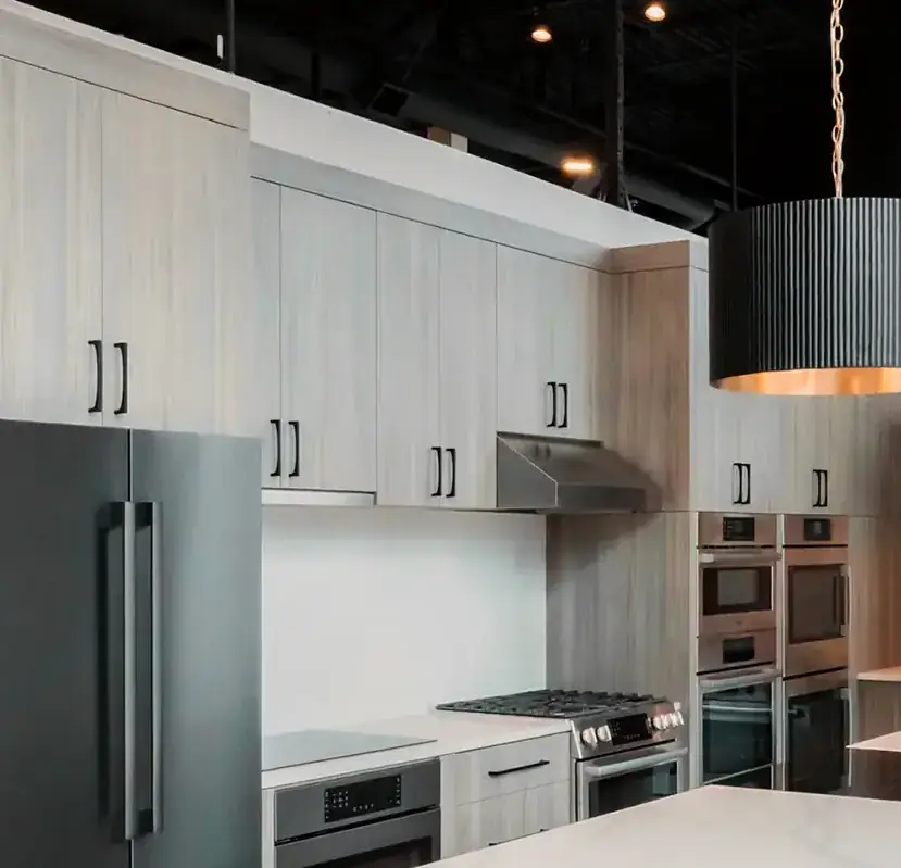 An appliance showroom lit by fluted pendants over a stone island, with track lighting and recessed downlights across a black open ceiling