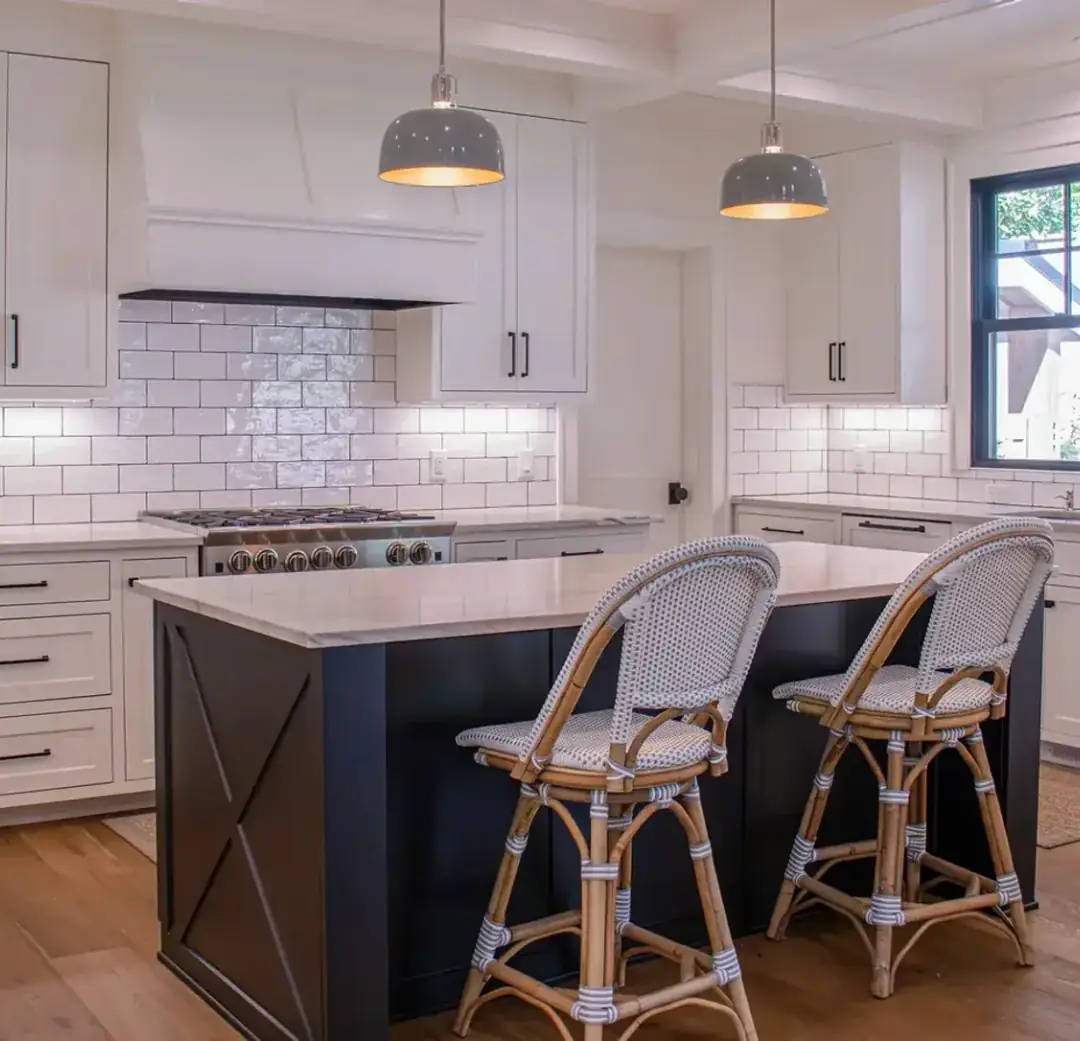 Finished kitchen in a new build — dome pendants over a navy island, under-cabinet lighting along the backsplash, and recessed cans in a coffered ceiling