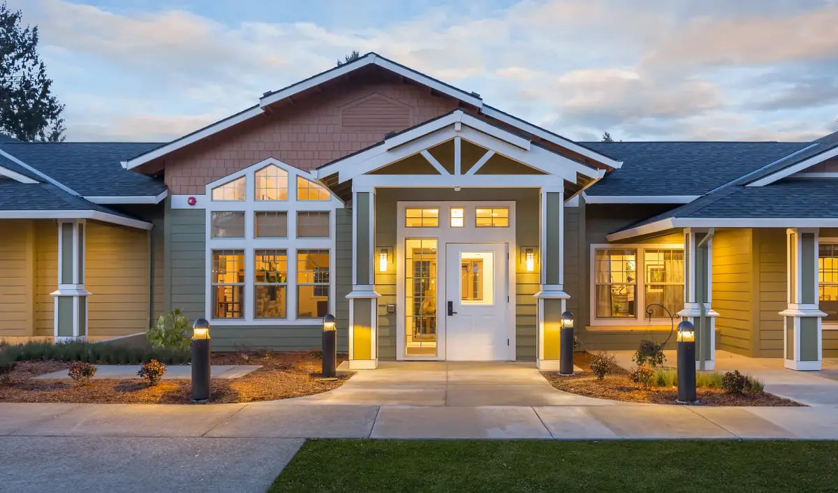 The entry of a craftsman-style building at dusk, lit by wall sconces, bollards along the path and warm interior light