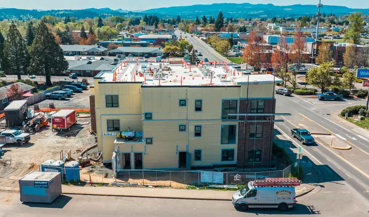 A three-story mixed-use building under construction from above, rooftop equipment stubbed out and a service van at the curb