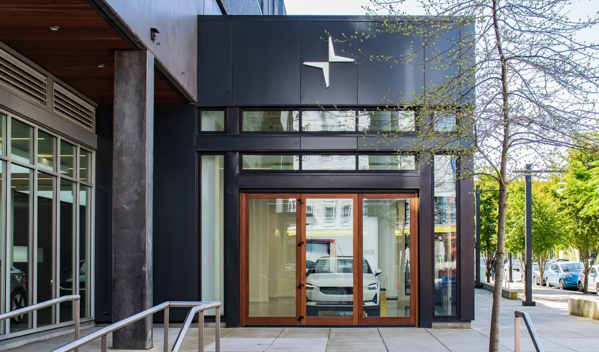 The dark-clad frontage of a car showroom, a lit interior and a white car behind full-height glazing