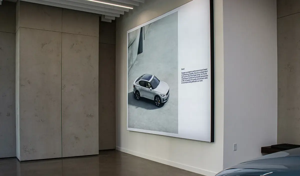 A large backlit lightbox display on a showroom wall, under a run of linear ceiling lighting