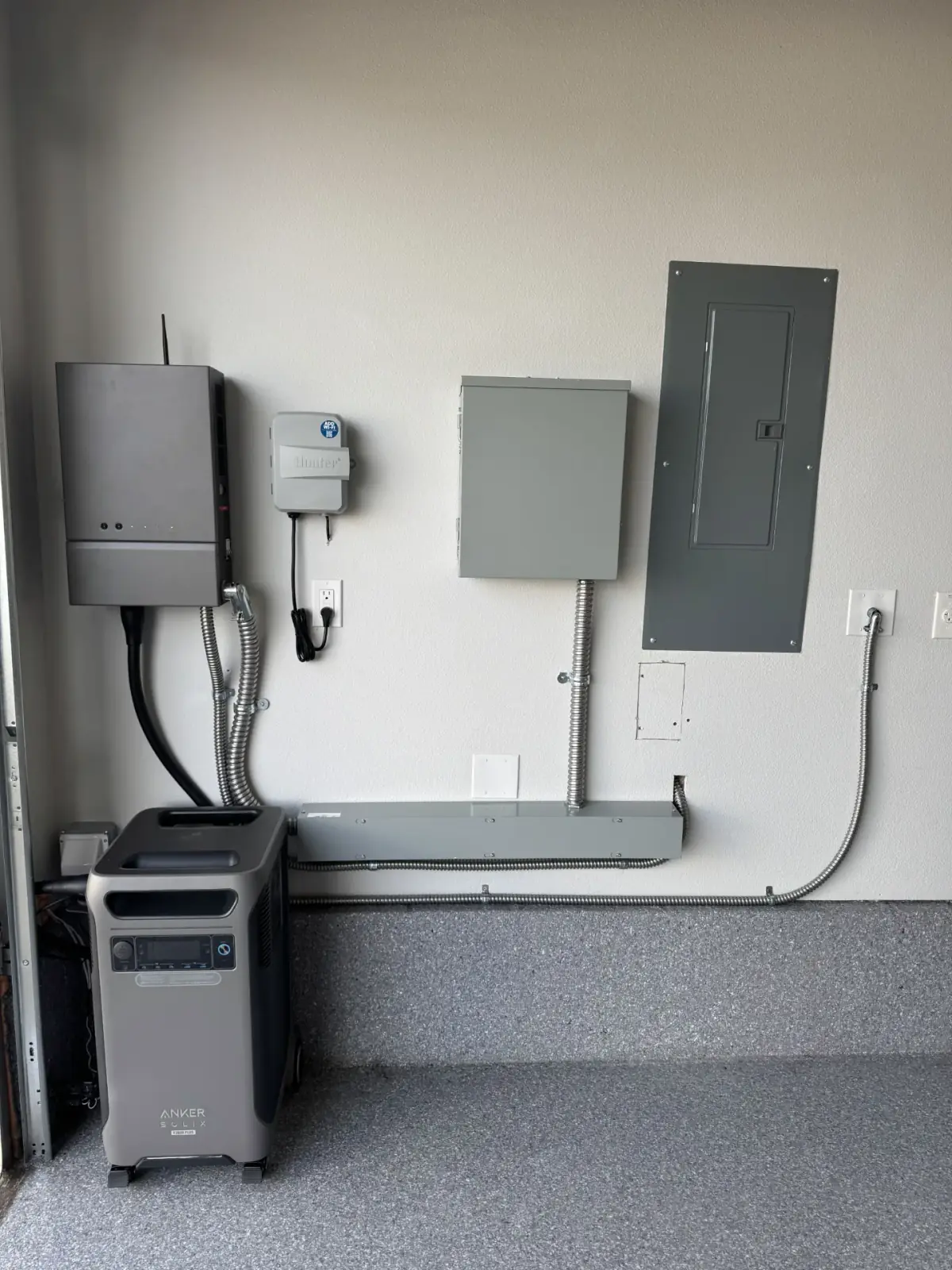A garage wall with an inverter, disconnect, load center and a portable battery unit below them