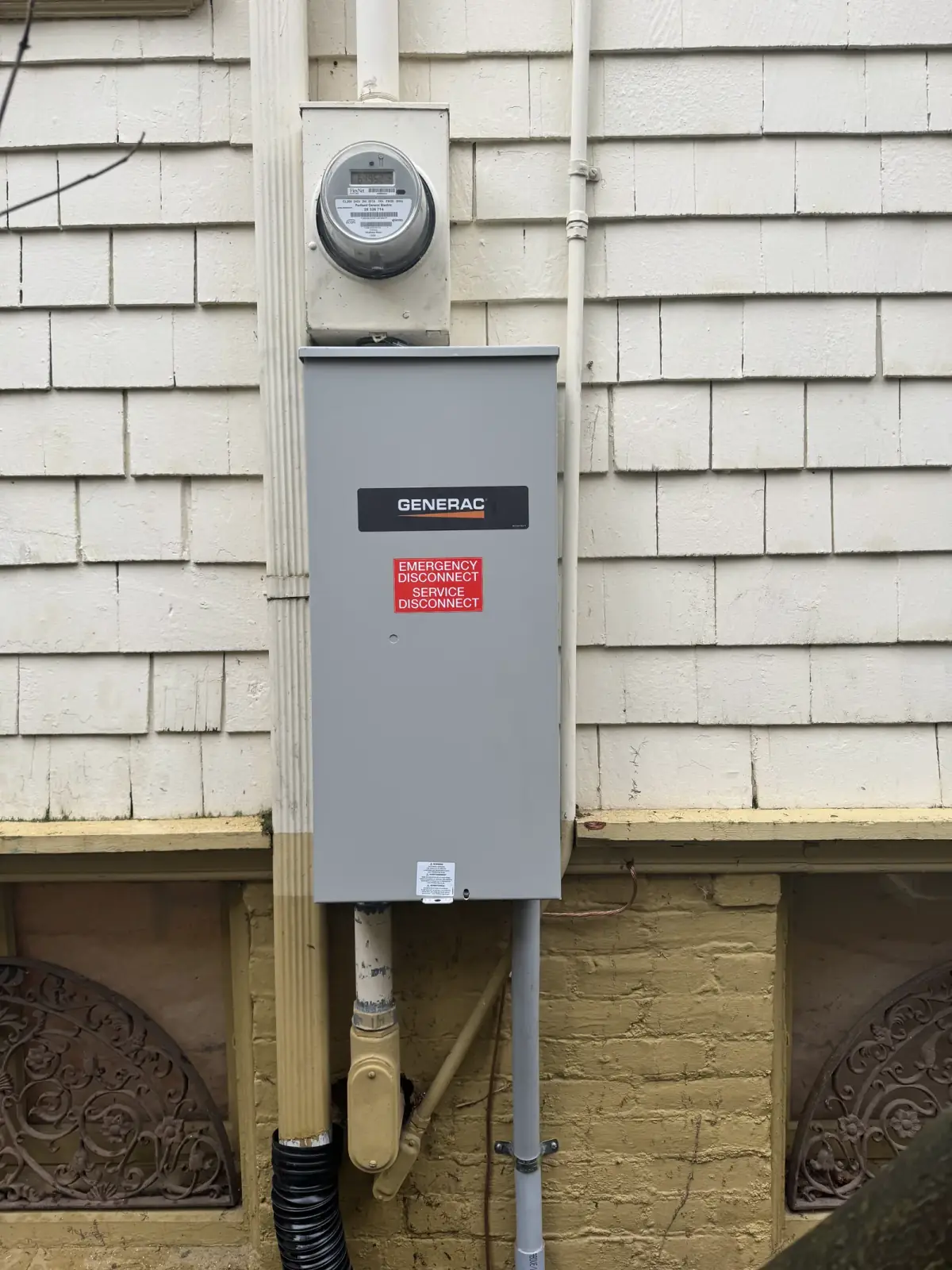 A Generac service disconnect under the meter on a shingled wall, conduit dropping to the crawlspace