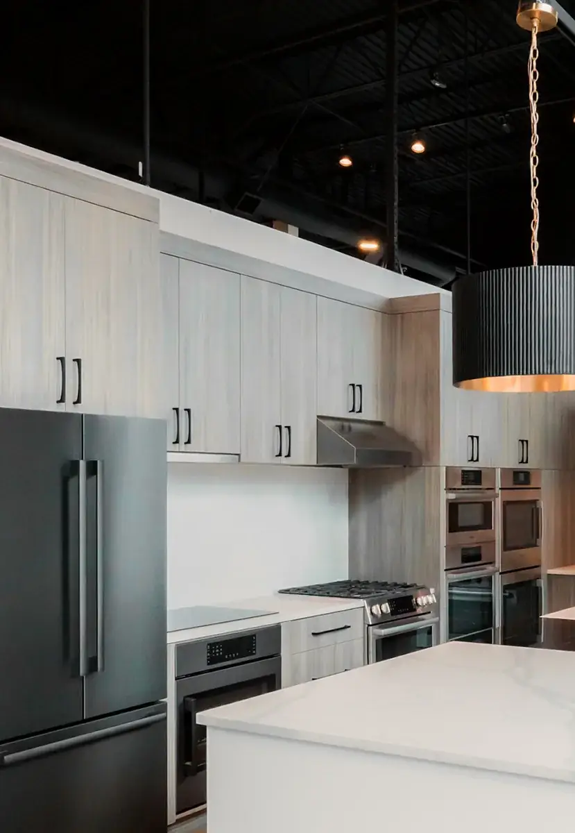 An appliance showroom lit by fluted pendants over a stone island, with track lighting and recessed downlights across a black open ceiling