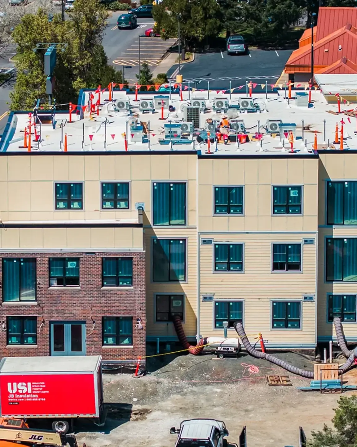 The same building mid-construction, rooftop penetrations and equipment set out across the roof while the exterior is being finished