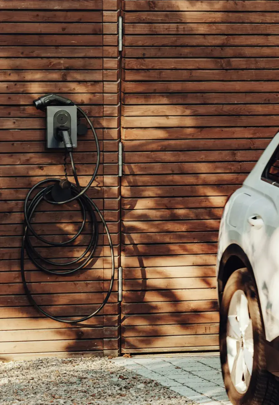 Wall-mounted EV charger with its cable coiled on a timber-clad garage wall, a white electric car parked alongside