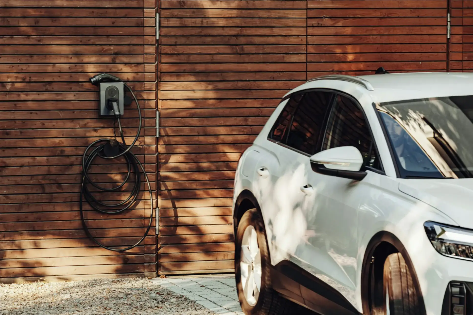 Wall-mounted EV charger with its cable coiled on a timber-clad garage wall, a white electric SUV parked alongside