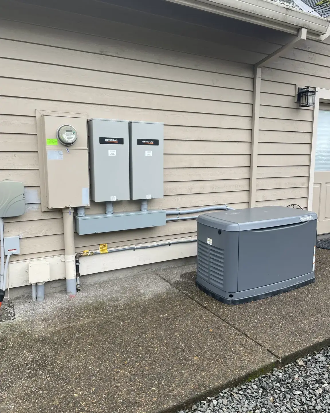 Meter, two Generac transfer switches and a gutter box on a lap-sided wall, with a standby generator on the driveway beside them