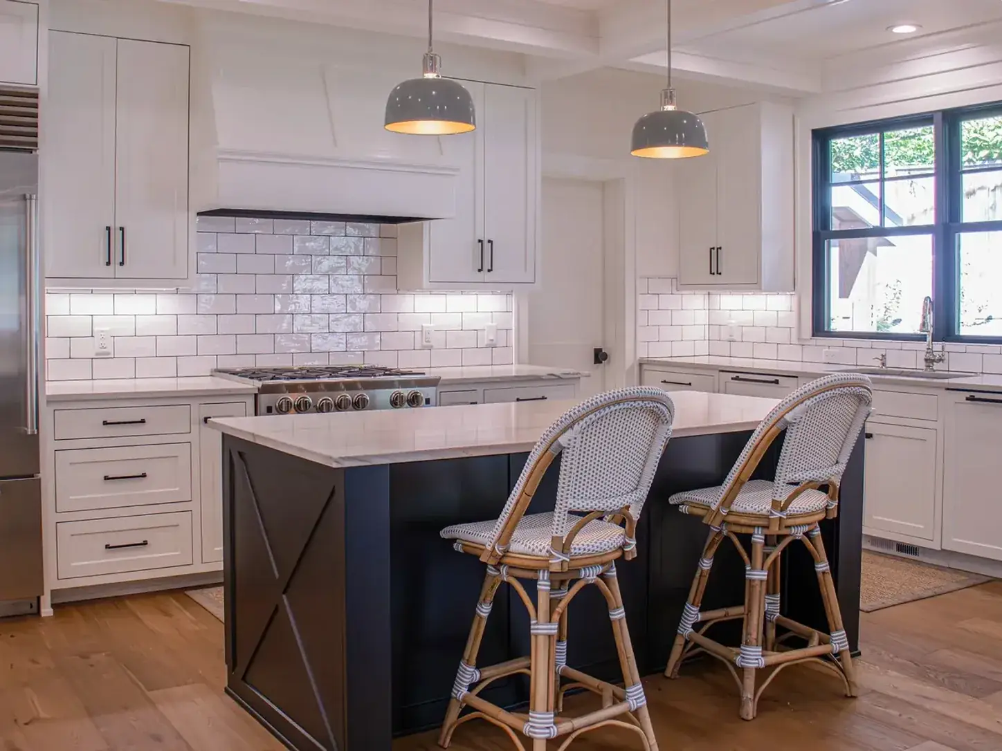Finished kitchen in a new build — dome pendants over a navy island, under-cabinet lighting along the backsplash, and recessed cans in a coffered ceiling